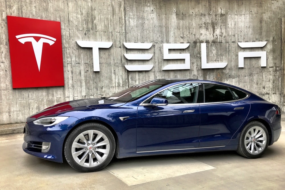 Tesla car displayed in front of a large TESLA sign, representing advancements in self-driving technology