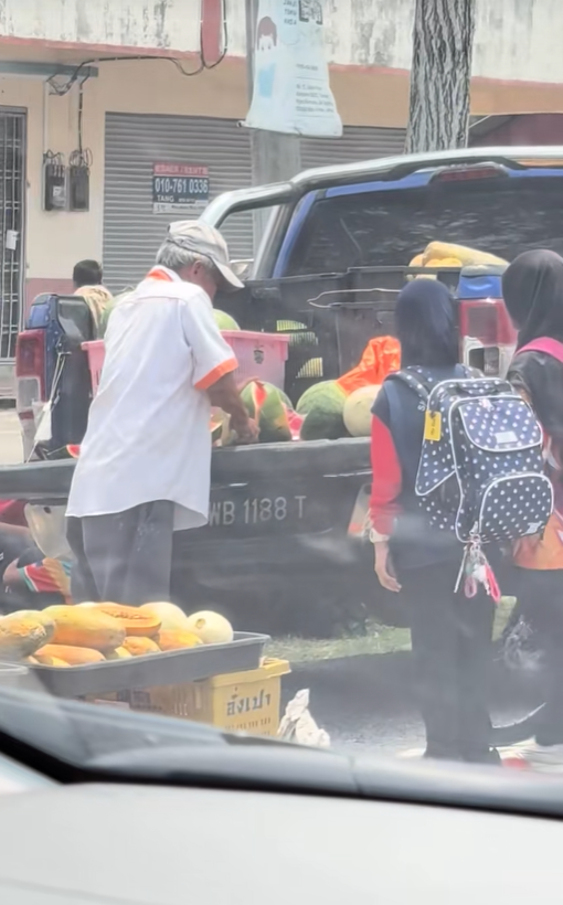 The uncle was slicing watermelon for children in front of the school